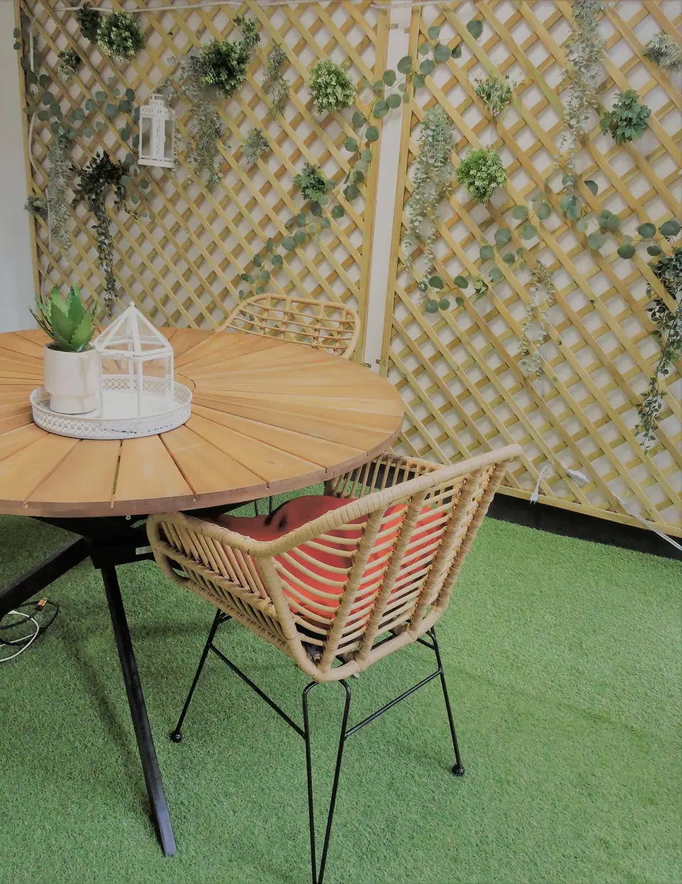 Wooden table and rattan chair on artificial turf in front of a lattice screen