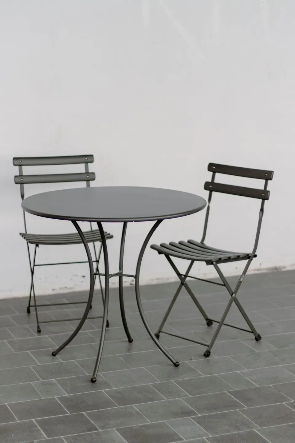 Small round metal bistro table with two folding chairs on a tiled floor
