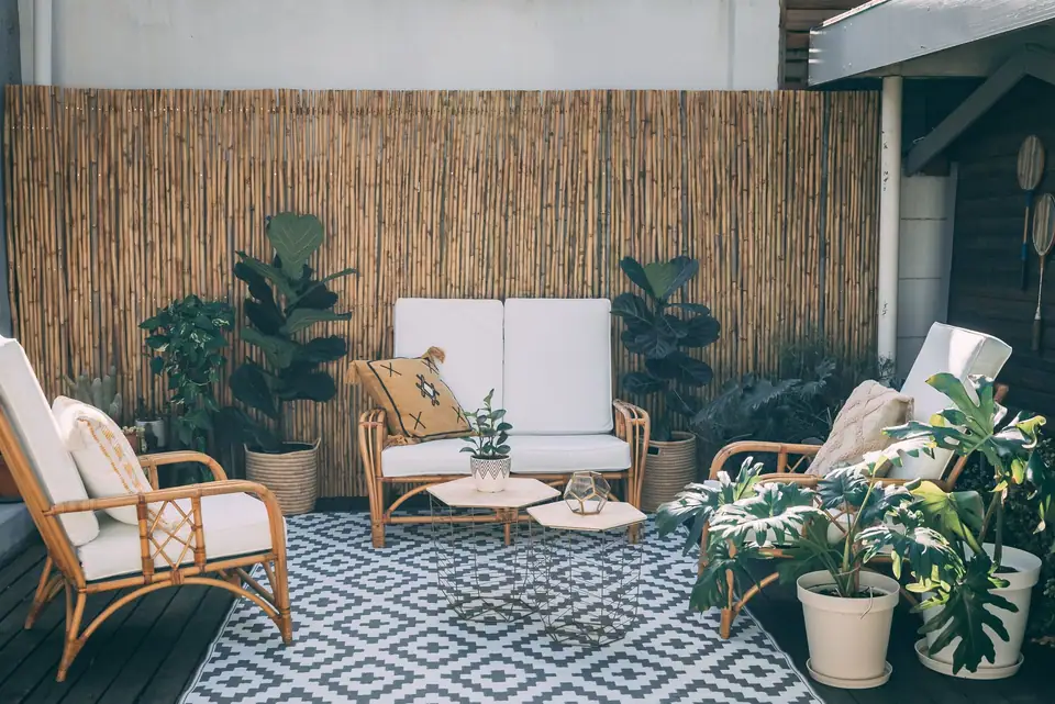 A small outdoor space with a patterned outdoor rug, rattan furniture, potted plants and a bamboo screen