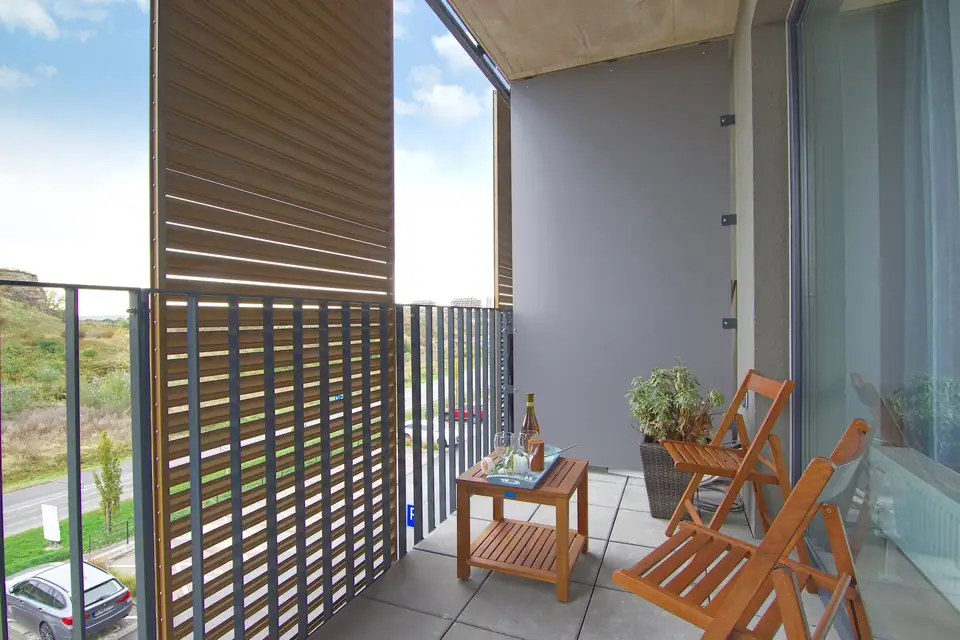 Modern balcony with a slatted wooden privacy screen, folding wooden chairs and a small table