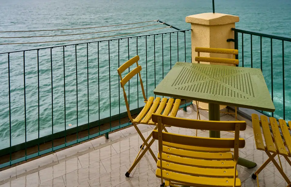 Yellow folding bistro chairs and a small table on a seaside balcony